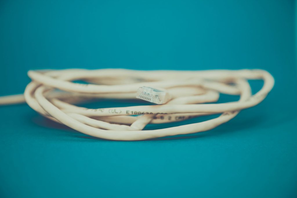A detailed close-up of a coiled Ethernet cable with an RJ-45 connector against a teal background. — 0975 What Network