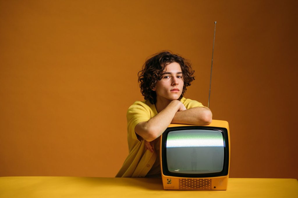 Trendy young man with curly hair in yellow fashion posing with an old TV set. — 12 51 Lyrics