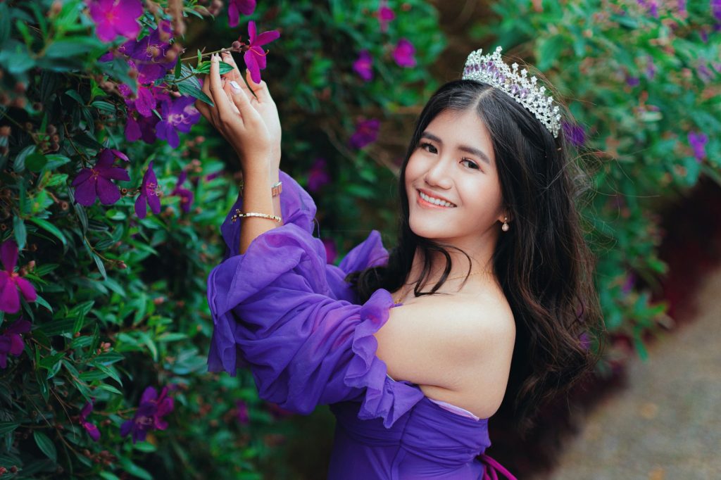 A smiling woman in a purple dress with a crown, surrounded by vibrant flowers. — Andrea Brillantes Scandal