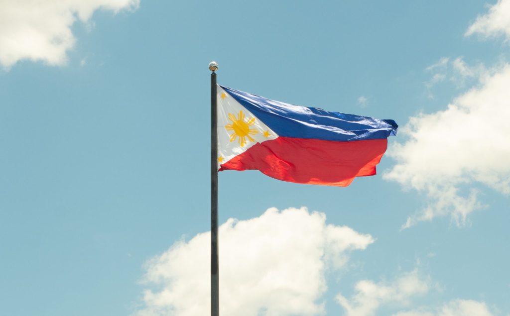 The national flag of the Philippines waving proudly in a clear blue sky with clouds. — Ano Ang