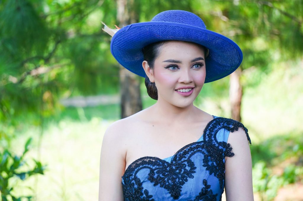 Charming woman in a stylish blue dress and hat, smiling outdoors amidst lush greenery. — Ara Mina Scandal