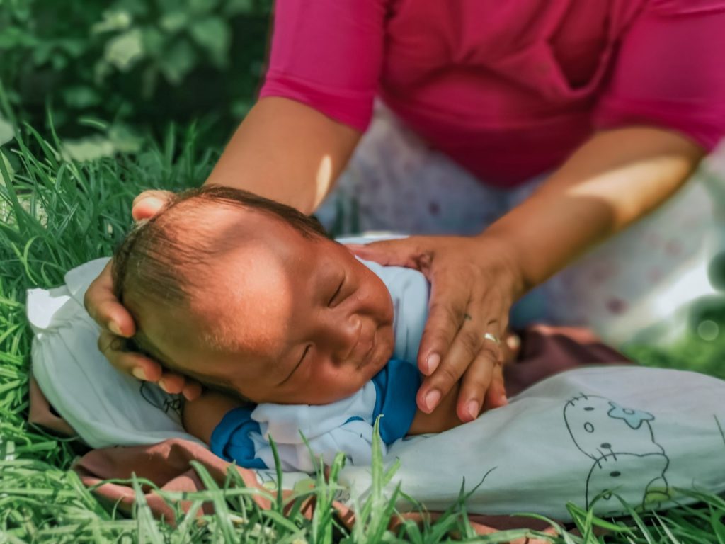 A peaceful baby lying on the grass being gently cared for by a woman. — Balita