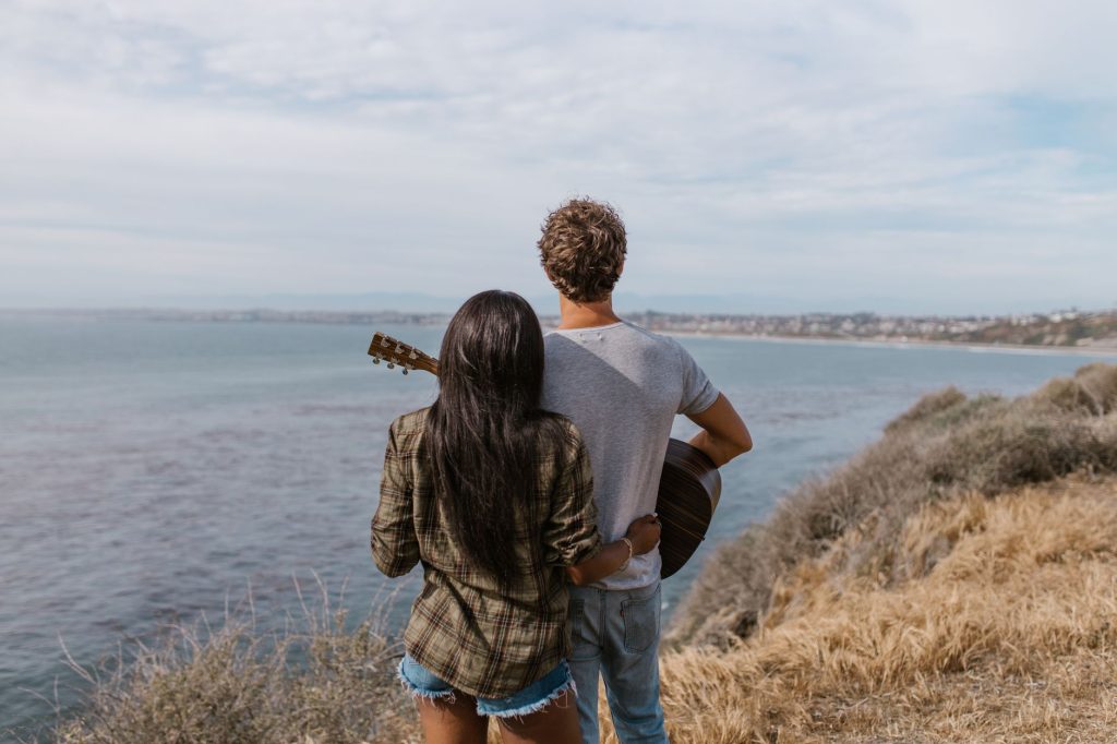 Couple embracing with guitar at ocean viewpoint, capturing intimacy and serenity. — Best Part Lyrics