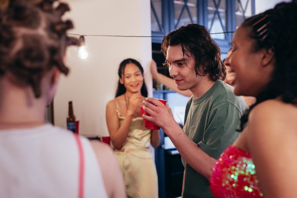 Smiling friends holding cups at a lively indoor party. — Collage Dorm Party