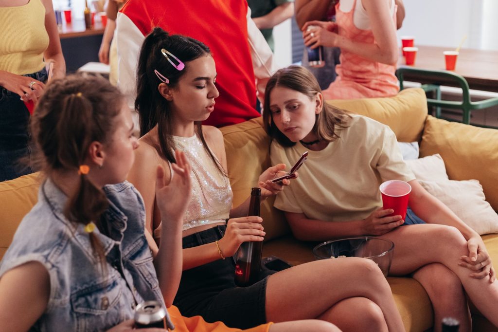 Young women at a casual house party chatting and using mobile phones. — Collage Dorm Party