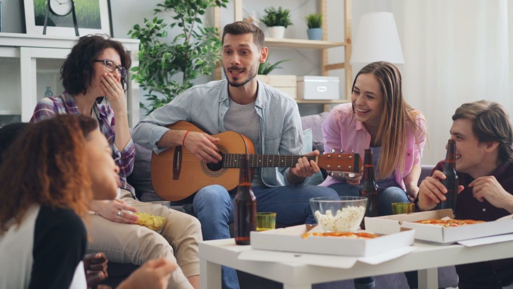 A joyful group of friends enjoying a casual indoor gathering with music and pizza. — Collage Dorm Party
