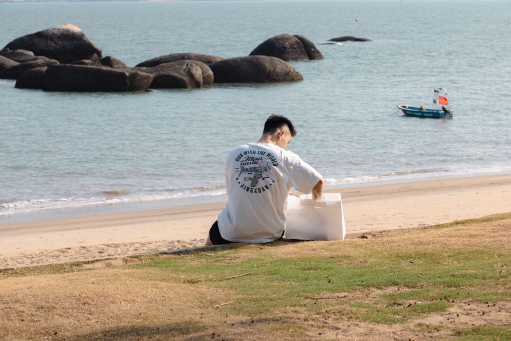 Man enjoying a peaceful day by the seaside in Xiamen, China with eco-friendly packaging. — Dbtk