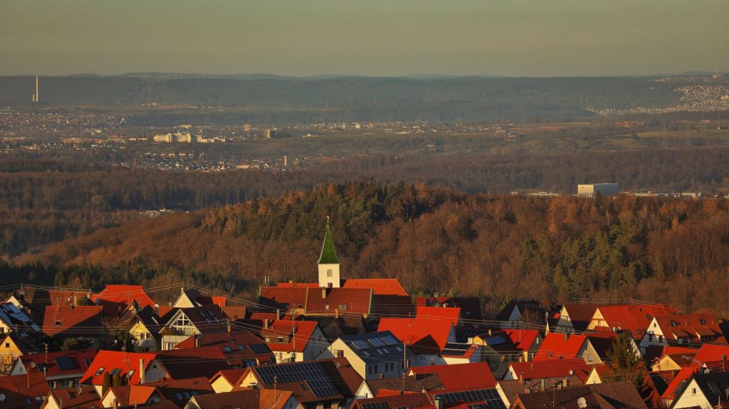 A scenic view of a quaint village surrounded by forests and valleys at sunset. — Felching