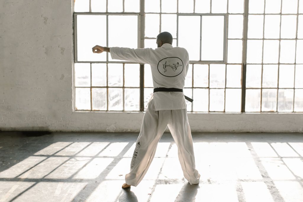 Man in karate uniform practicing punches in a sunlit room with large glass windows. — Genyo