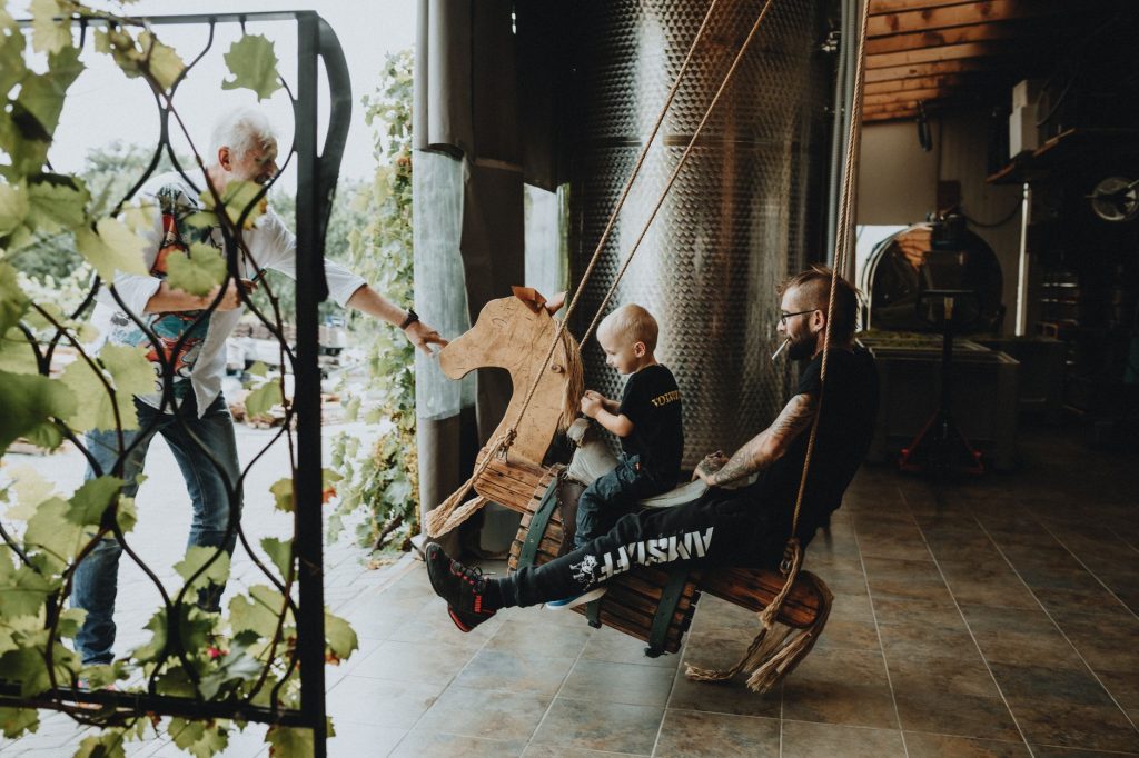 A father and his child enjoy a playful moment on an indoor wooden swing in a rustic setting. — Hintai
