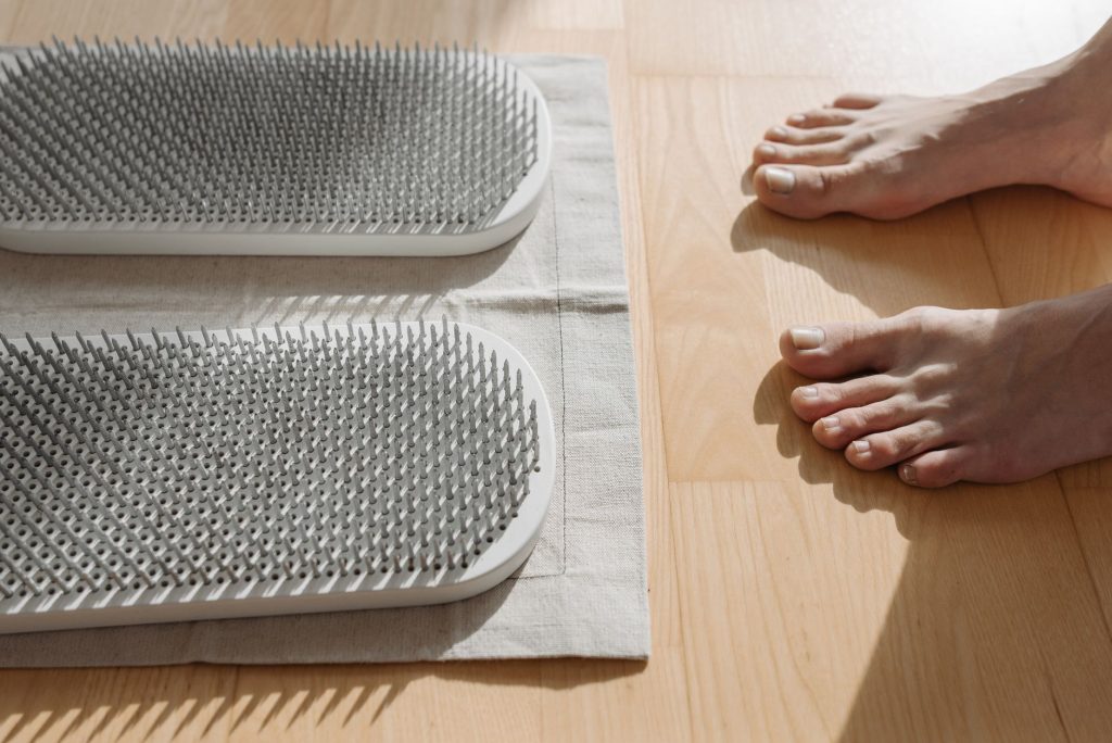 A pair of bare feet near a metal sadhu board on a wooden floor for therapeutic use — Itotan