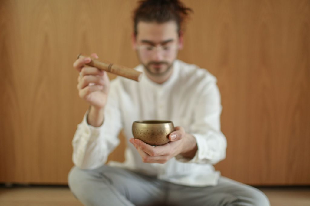 A man meditating indoors with a Tibetan singing bowl, promoting relaxation and mindfulness. — Iyotan