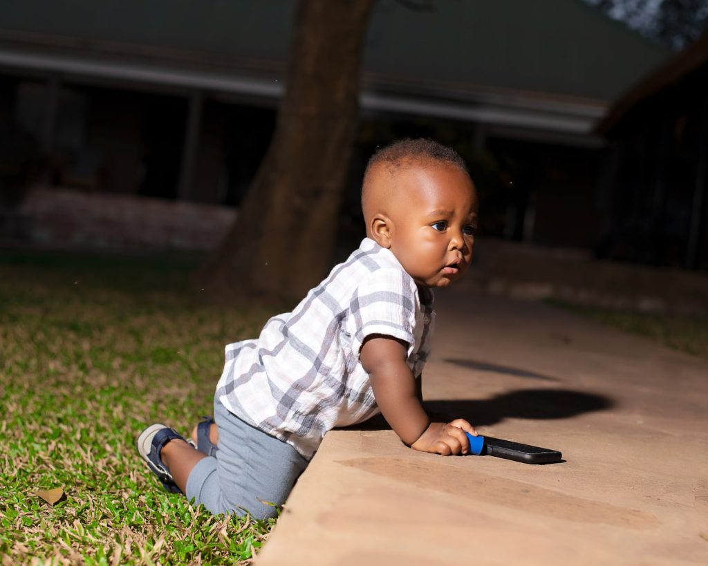 Adorable baby crawling on pathway with toy during a sunny day outdoors. — Iyotan