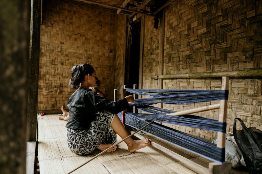An adult woman weaving on a loom indoors in Banten, Indonesia. — Kantutan