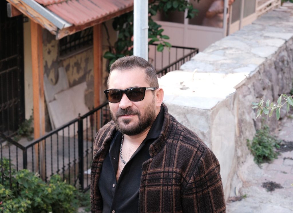 Stylish man wearing sunglasses and plaid jacket standing outdoors on a sunny day. — Kayatan Com