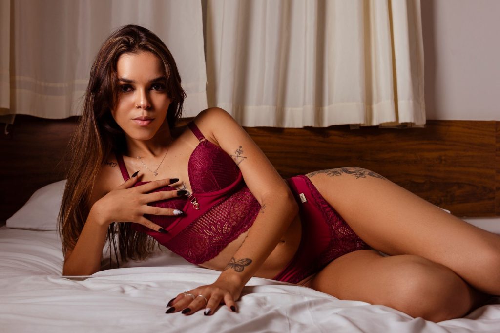 Woman in burgundy lingerie posing confidently on a bed, showcasing tattoos and elegance. — Kayatsex
