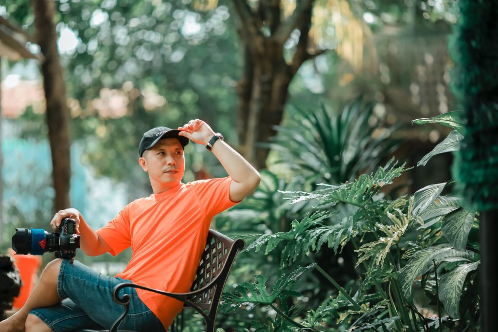 Candid shot of a photographer resting in a vibrant garden with camera gear. — Mang Kanor