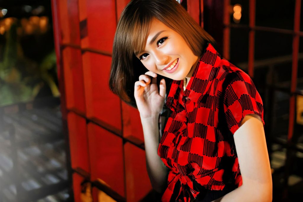 A vibrant portrait of a woman smiling in a red dress, set against an urban backdrop at night. — Mang Kanor Scandal