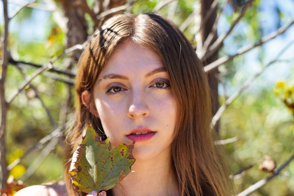 A serene portrait of a young woman holding a leaf, surrounded by nature. — Melody Marks