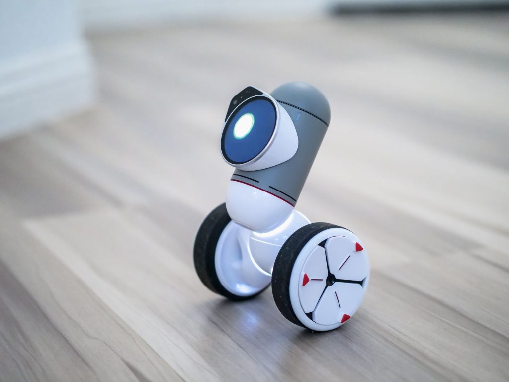 Close-up of a modern toy robot with wheels on a wooden floor, emphasizing its design and technology. — Multo