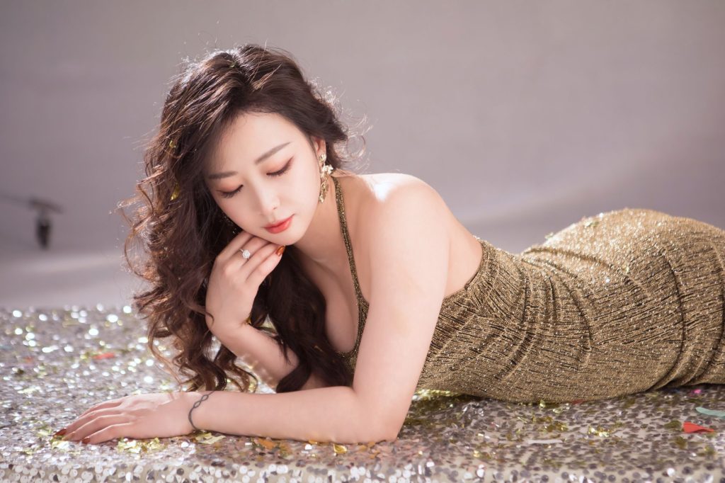 A graceful woman in a shimmering gold dress posing against a glittery background. — Mwplay888