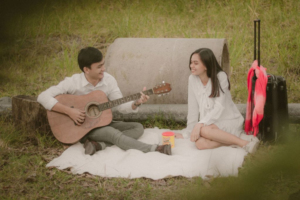 A couple enjoying a romantic picnic with guitar music in a serene park setting. — Paraluman Lyrics
