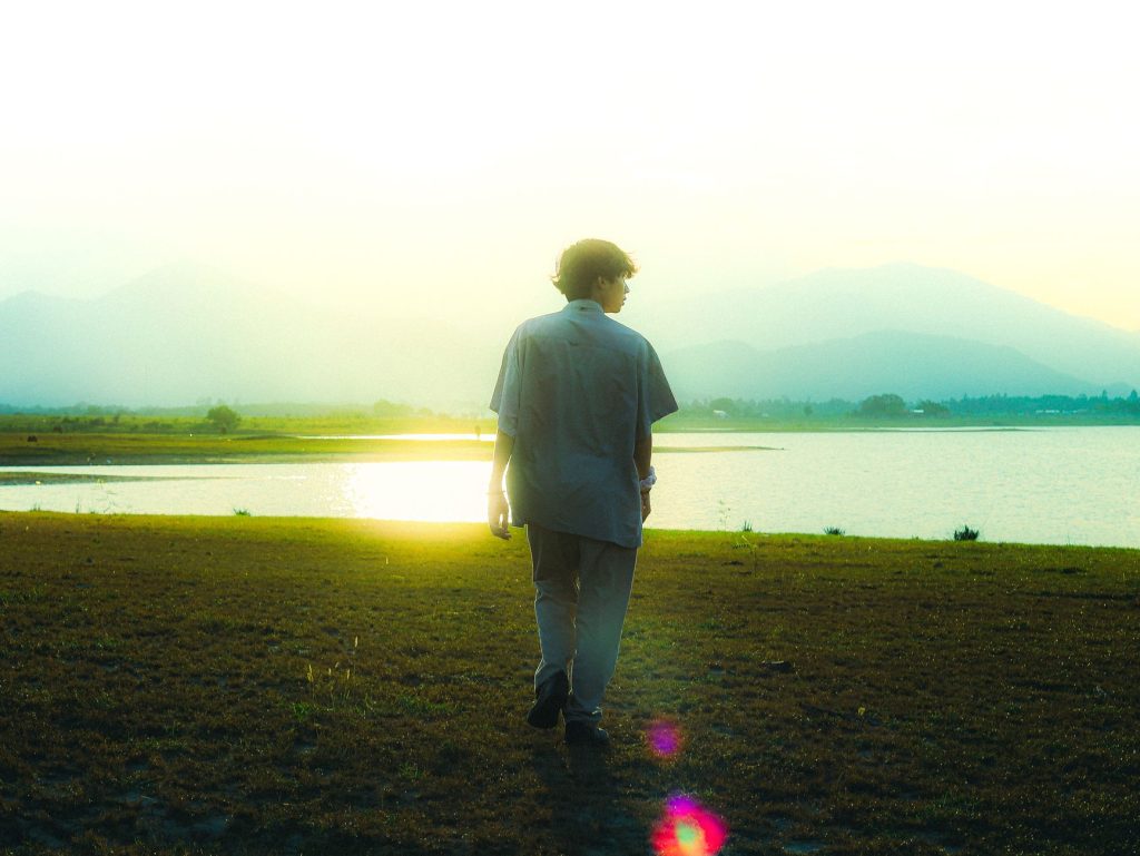 A young man walks by a tranquil lake during sunset, embodying peace and reflection. — Paraluman Lyrics