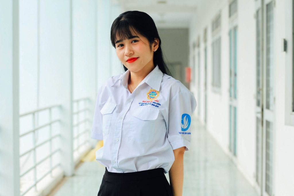Asian woman in a white button-up shirt smiling in an indoor hallway setting. — Penay Kantotan
