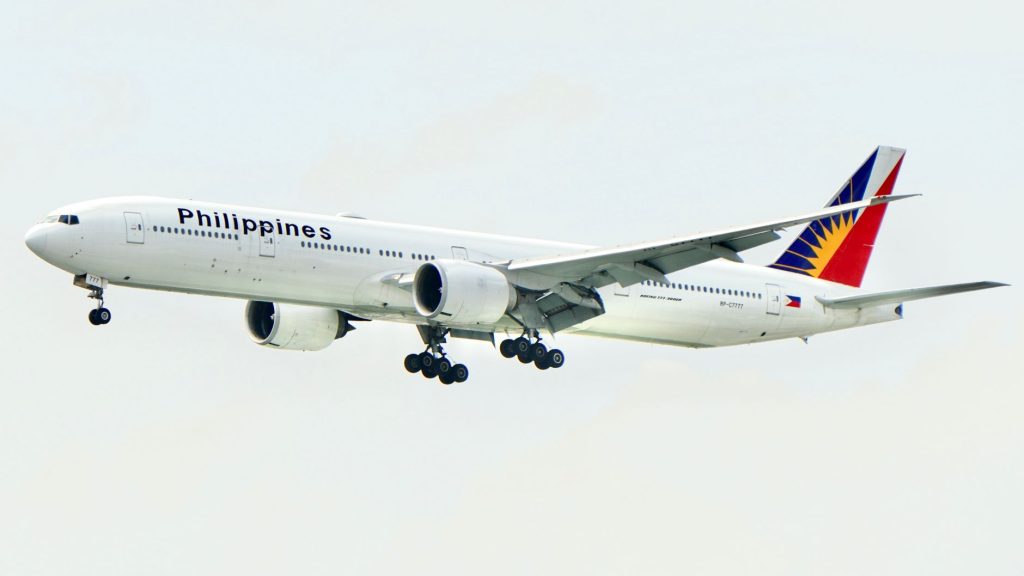 A Philippine Airlines Boeing 777 aircraft flying with landing gear lowered against a clear sky. — Philgeps