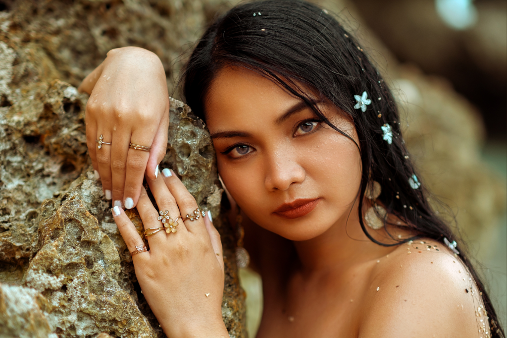 Woman posing against rock wearing elegant jewelry with natural makeup and floral accents. — Pinay Finger