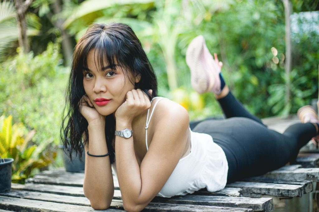 Young woman in tank top and leggings lying on wooden bench outdoors, looking at camera. — Pinay Flex
