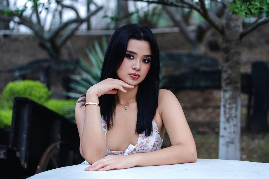 A serene portrait of a young woman sitting at a table outdoors, surrounded by nature. — Pinay Scandal