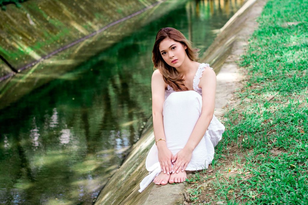 A serene portrait of a woman in a white dress sitting by a peaceful river, showcasing elegance and tranquility. — Pinay Viral