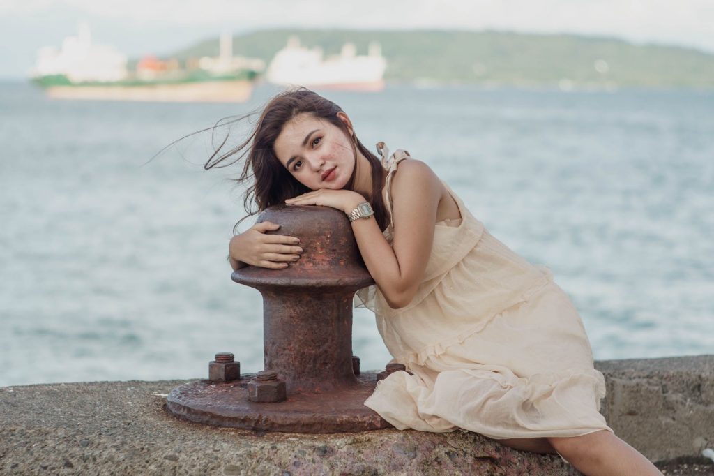 Peaceful dreamy female in light dress relaxing on stone border of waterfront and leaning on bollard — Pinayfkix