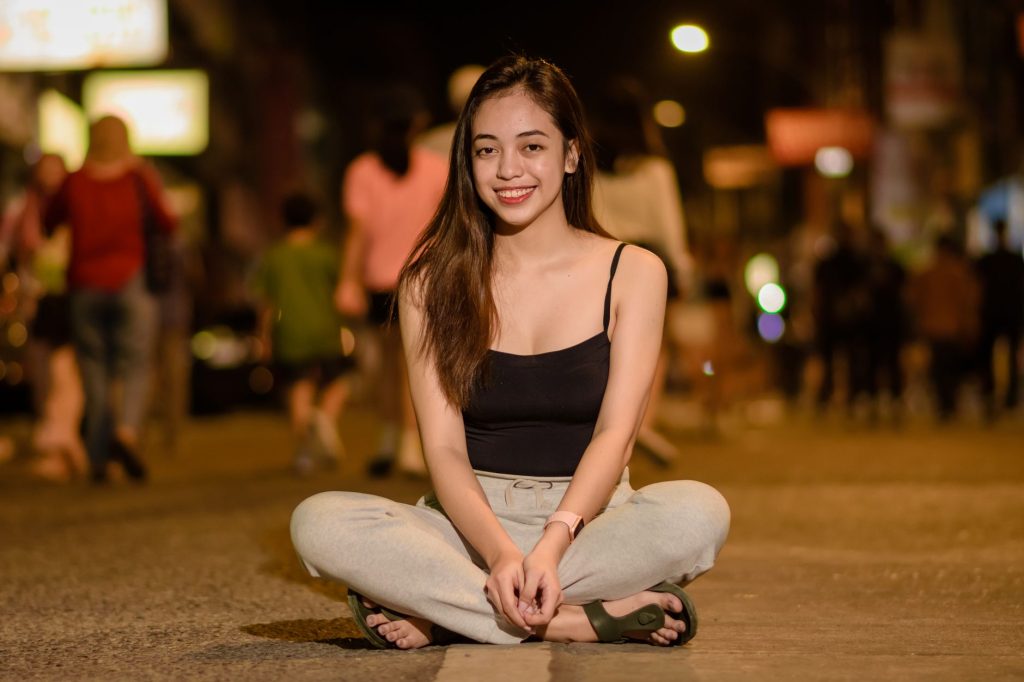 Young woman sitting and smiling on a city street at night, wearing casual attire. — Pinaysex Scandal