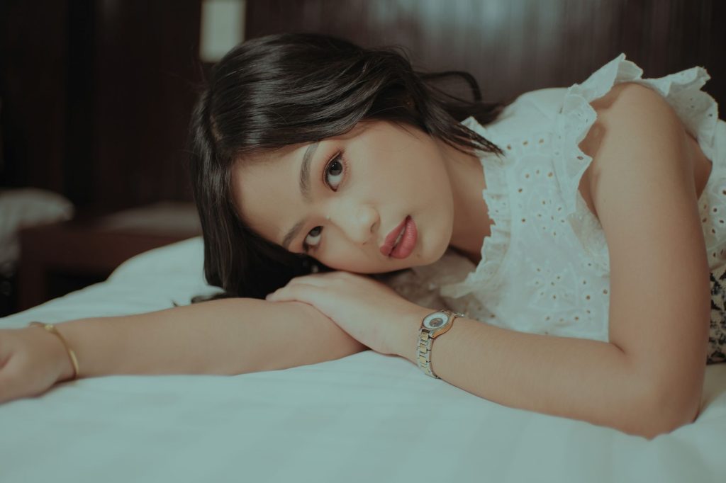 Calm young Asian woman with dark hair in stylish clothes lying on soft bed and looking at camera — Pinayvids