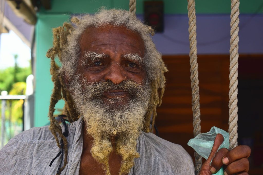 Close-up portrait of an elderly man with dreadlocks and a warm smile, embracing rustic charm. — Rastaman