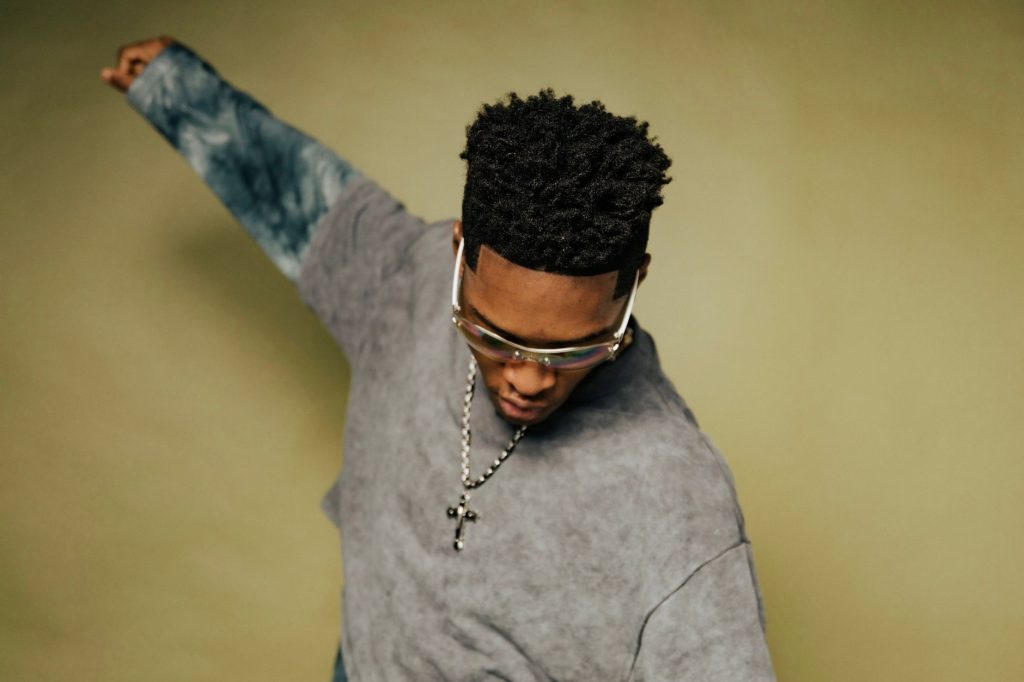 A fashionable young man with sunglasses and a cross necklace posing confidently. — Rbreezy