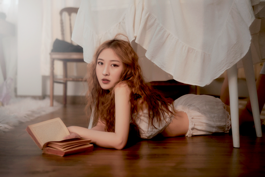 A young woman in a relaxed position indoors, reading a book on the floor with a dreamy expression. — Rule 34 Kpop