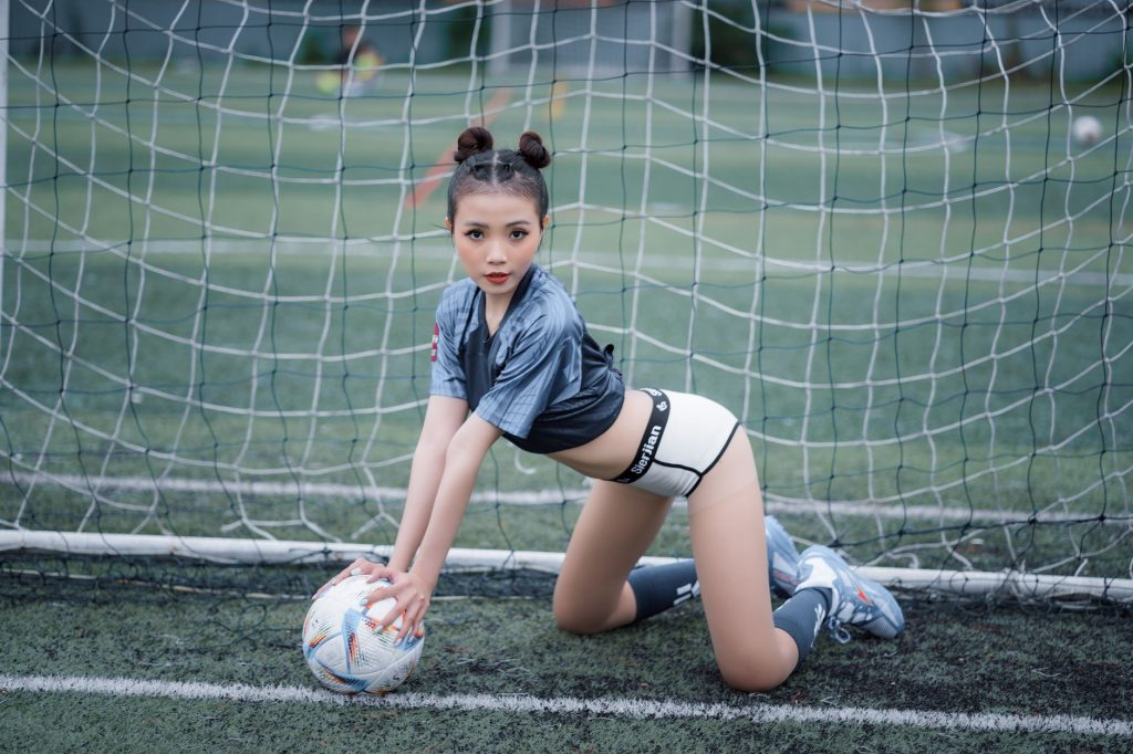 Fashion photoshoot of a woman in sportswear posing with a soccer ball on a football field. — S888 Live