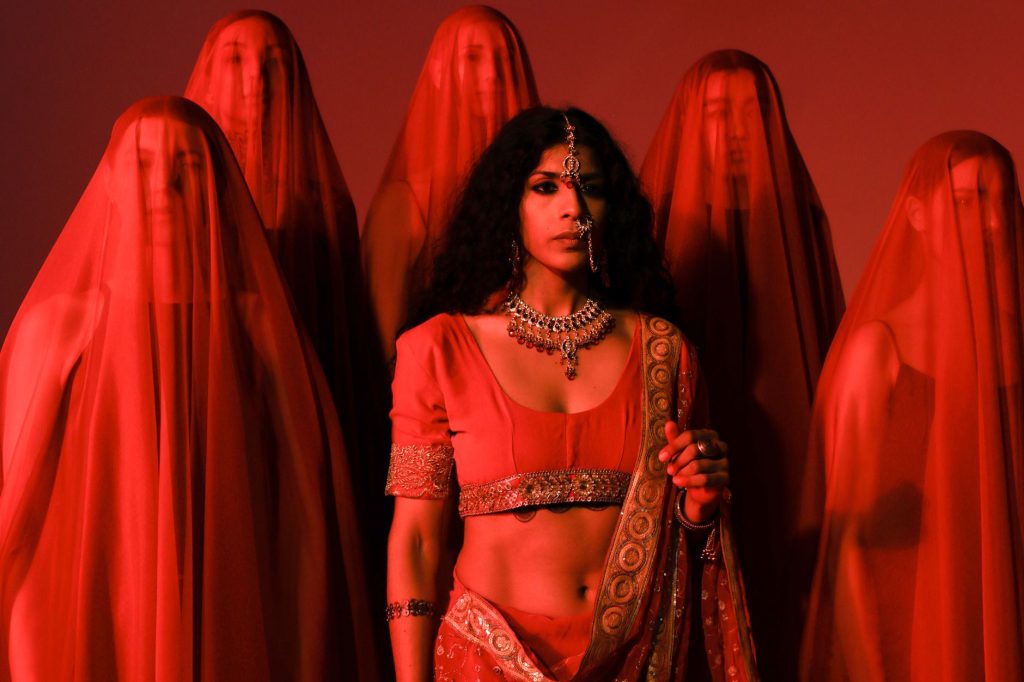 Artistic portrait of women in red traditional attire with veils, conveying cultural elegance. — Sana Lyrics