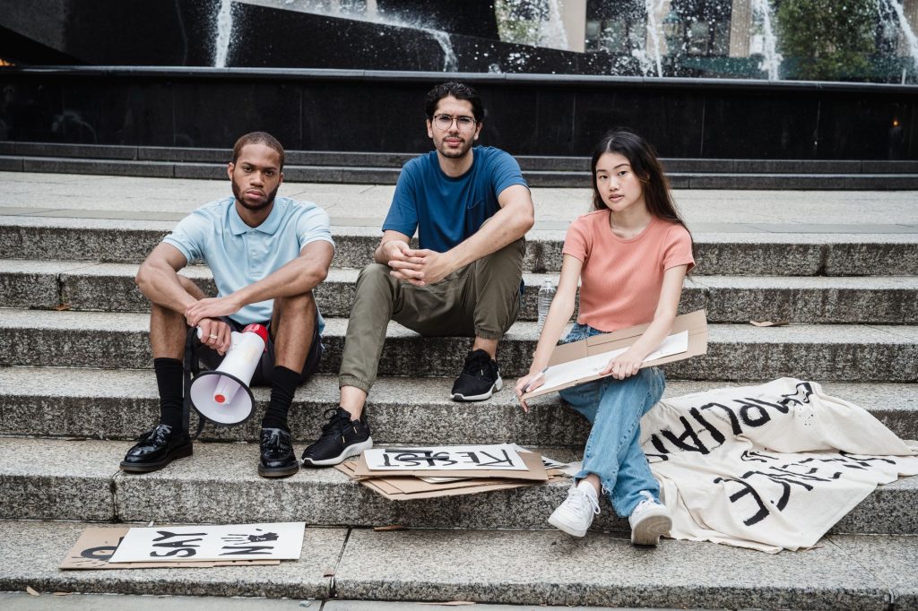 Three young activists with protest signs seated on concrete steps, symbolizing unity and peaceful protest. — Sayout