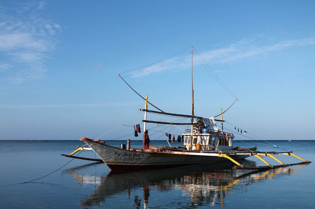 A traditional Filipino banca boat reflected in serene waters under a blue sky. — Spanish To Tagalog