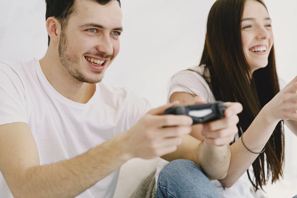 Crop happy man in white t shirt and jeans playing game pad while sitting with cheerful girlfriend in apartment on weekend — S