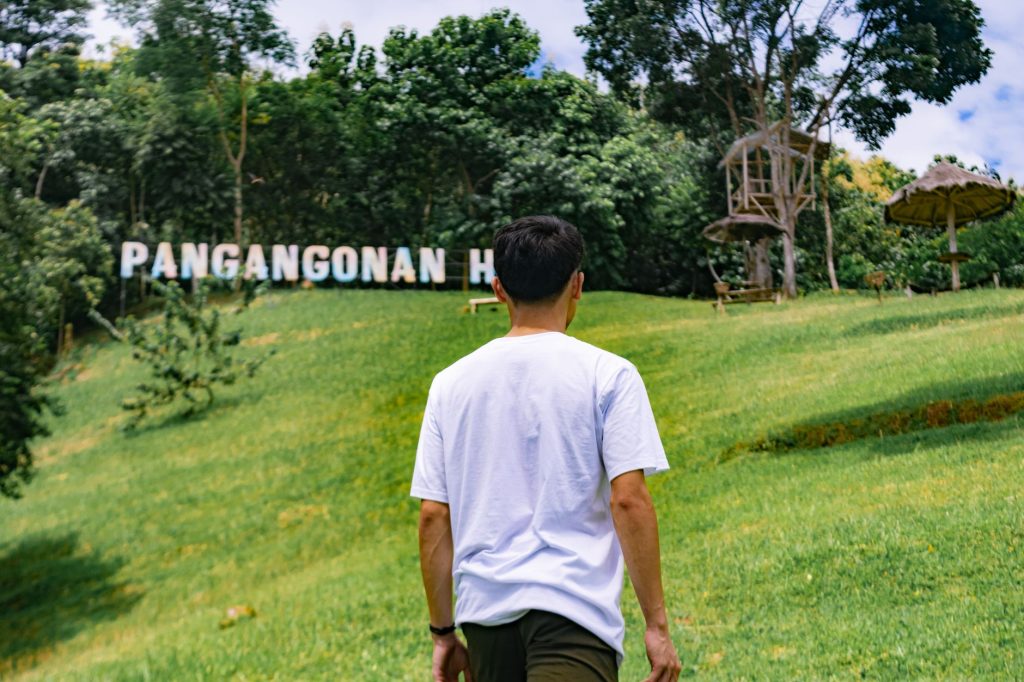 A person walking towards Pangangonan Hill, surrounded by lush greenery and a bright sky. — Tahanan Lyrics