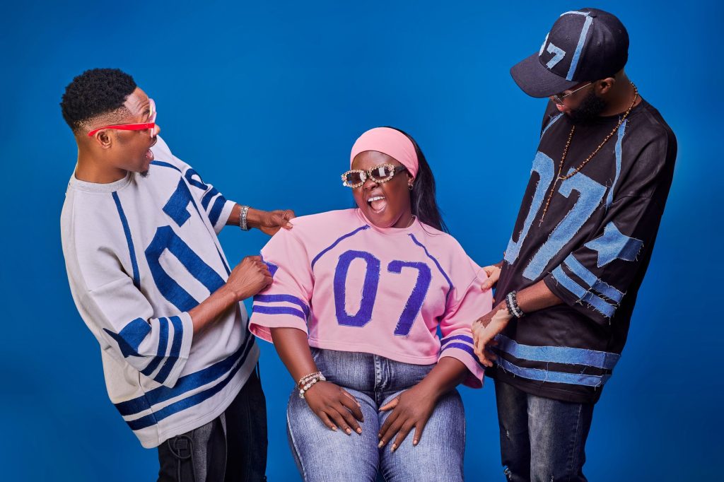 Three friends sharing a laugh, each wearing vibrant shirts with '07' prints on a blue background. — Ujizz