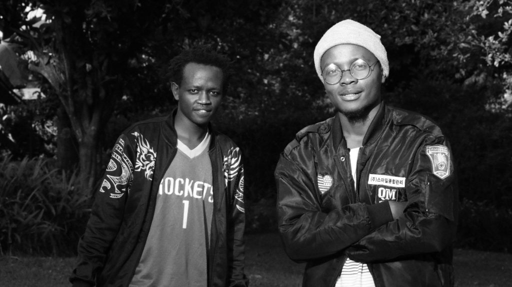 Black and white photo of two young men in stylish outfits outdoors, showing camaraderie. — Yuo